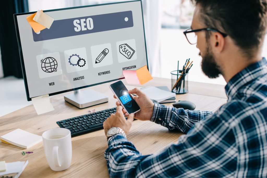 bonito jovem gerente seo usando smartphone e computador no local de trabalho